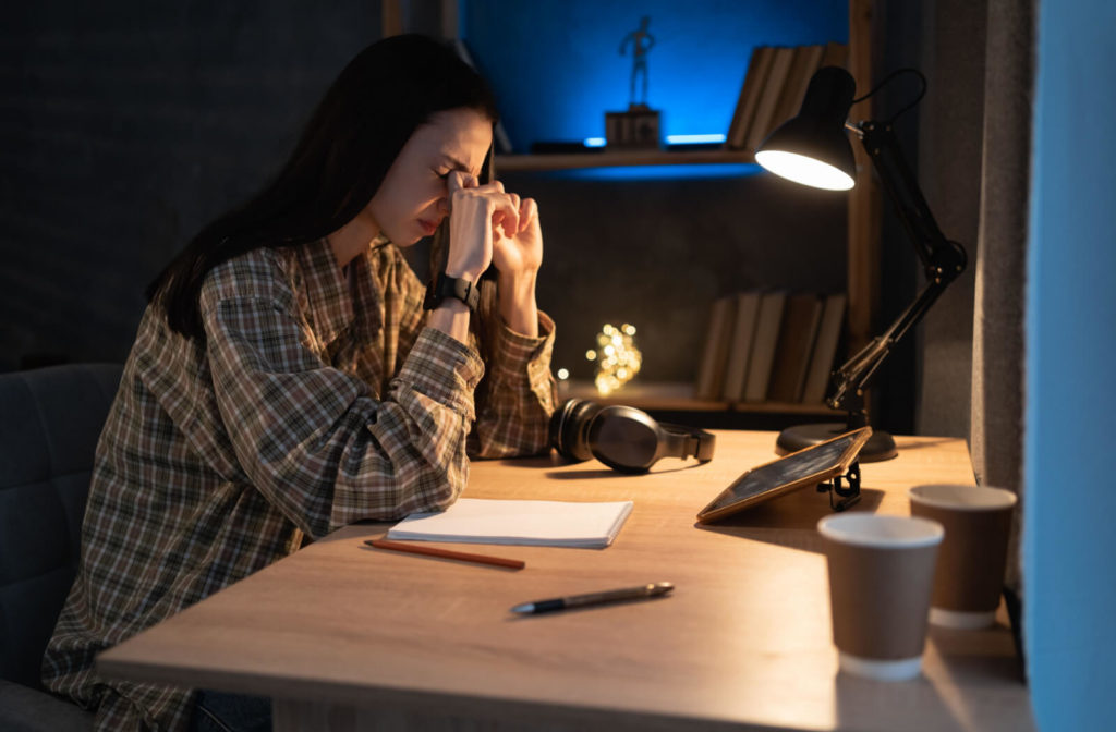 A female student is massaging her tired eyes after long exposure to blue light from her tablet pc at home doing homework.