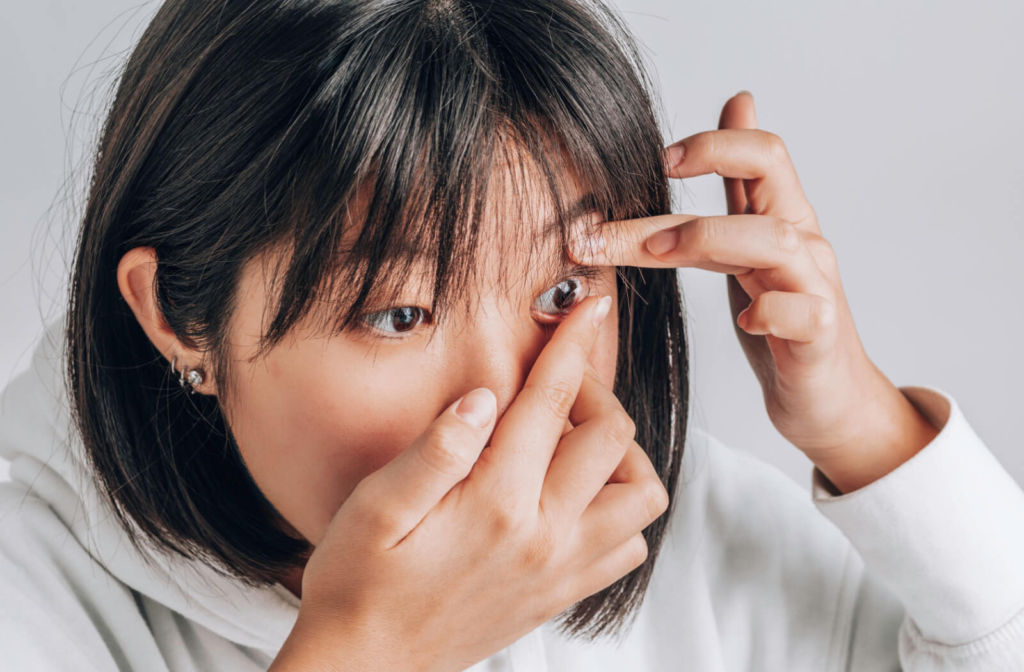 A woman using her fingers to lift her upper eyelids while inserting contact lenses onto her eyes.
