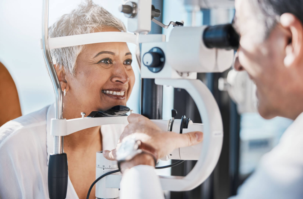 A male optometrist examines a smiling senior woman's eyes.