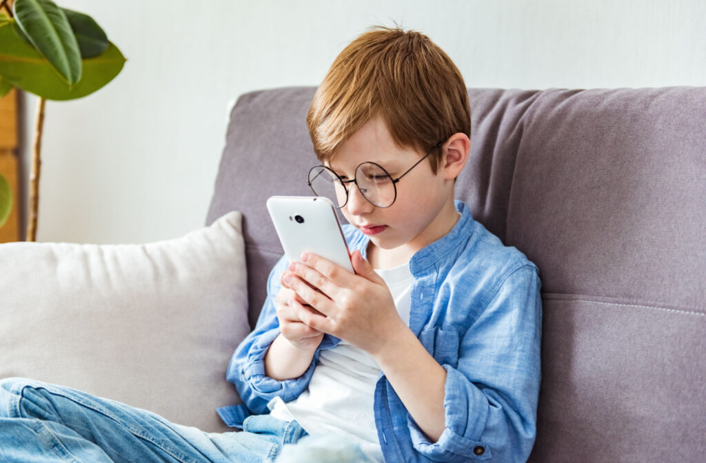 A child with glasses holding his smartphone very close to his face