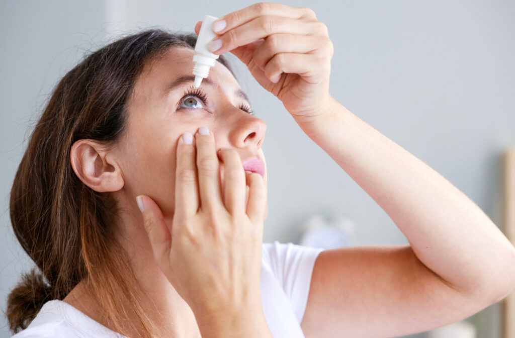 Close up of a younger woman applying eye drops to her right eye.