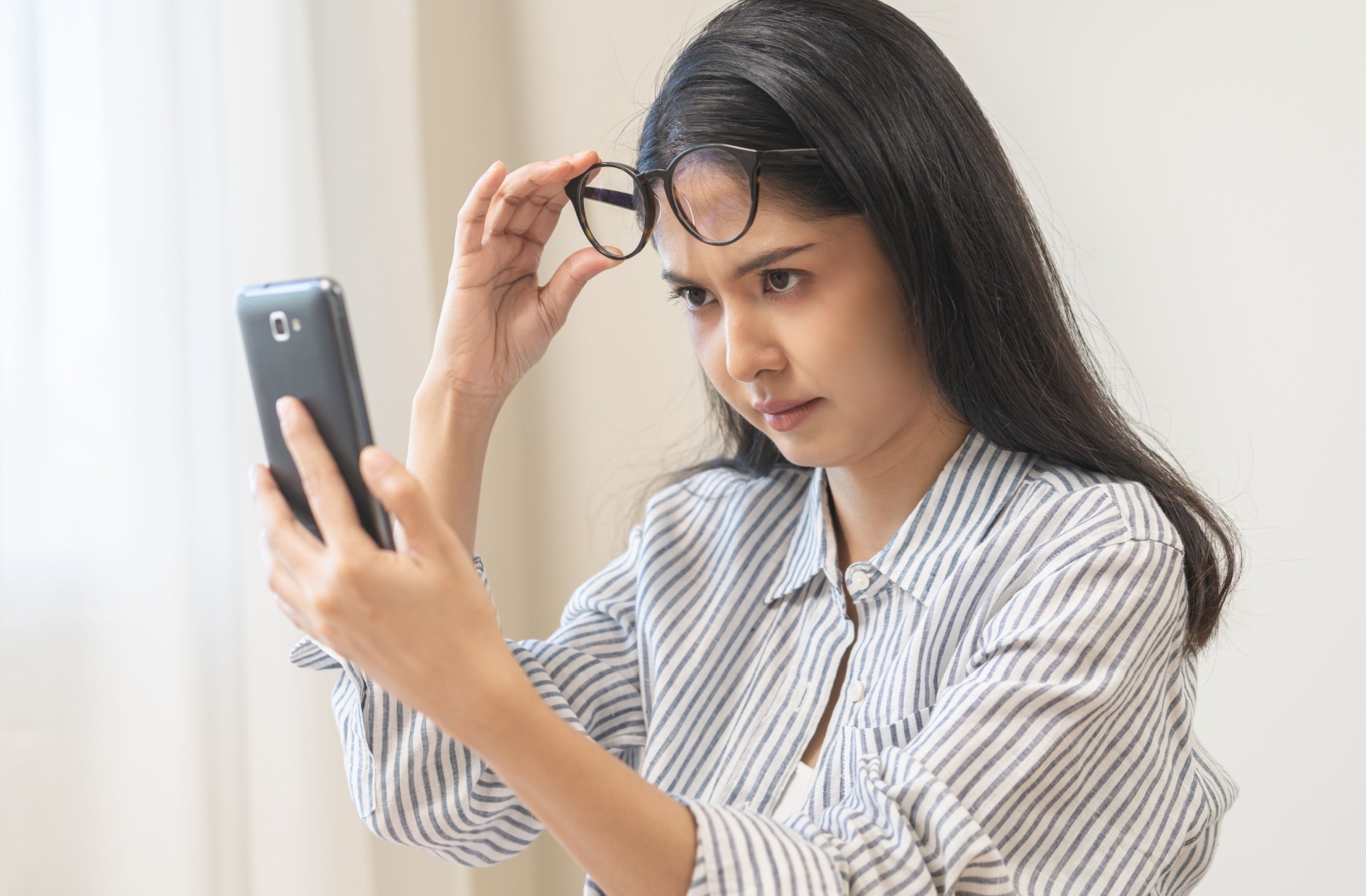 A woman is having difficulty reading the words on her smartphone due to presbyopia.