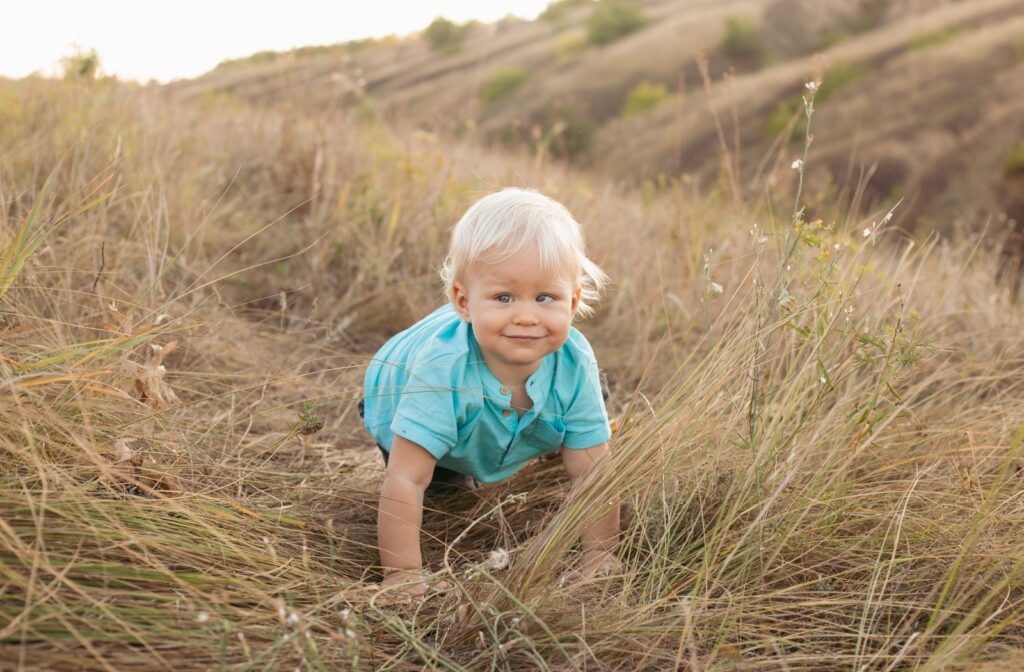 Smiling toddler crawling in a grassy field on a sunny day, showcasing natural curiosity and exploration.