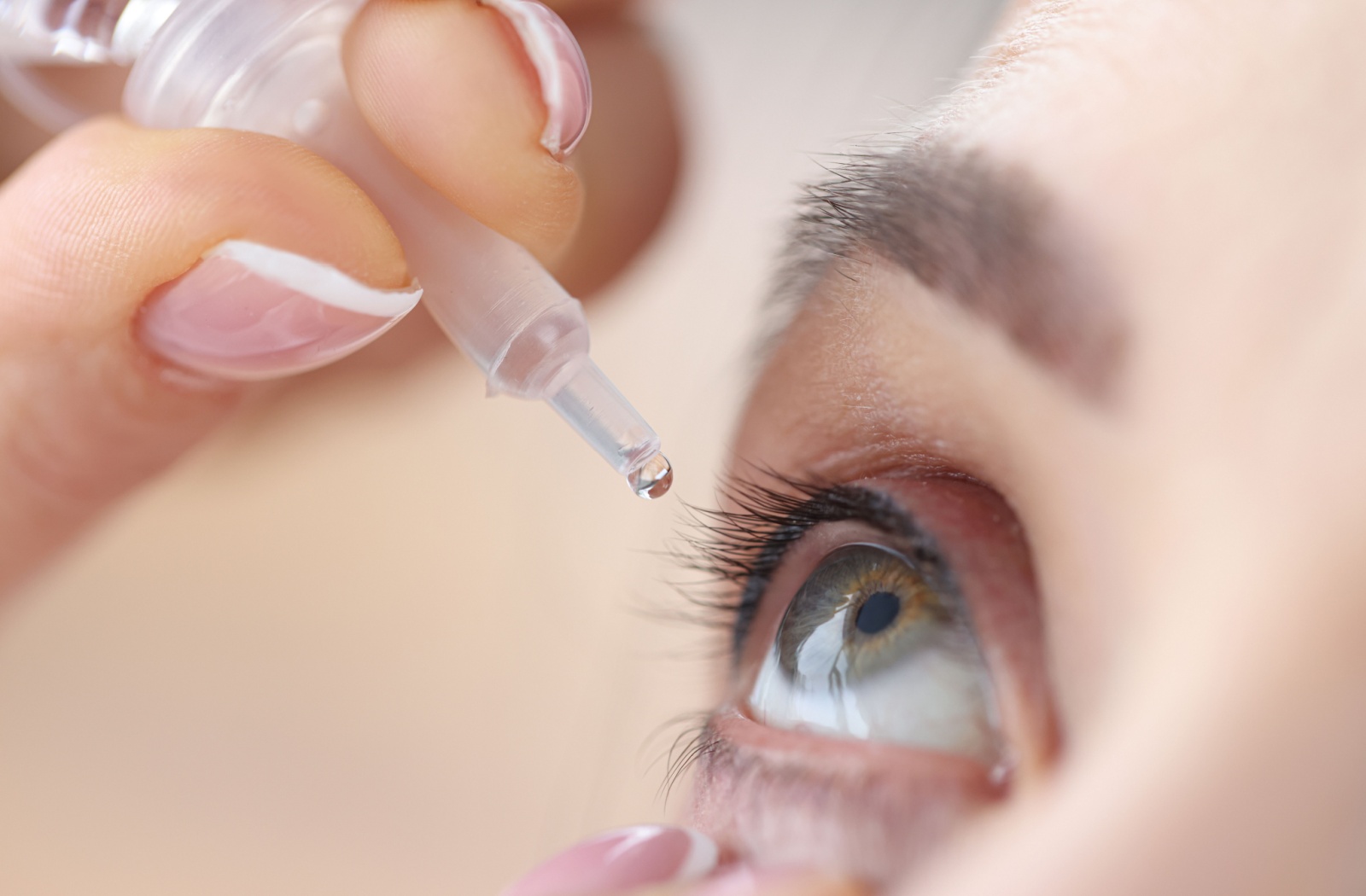 A close-up of a woman pulling down on her face and dripping prescription hyaluronic acid eye drops into her eye.
