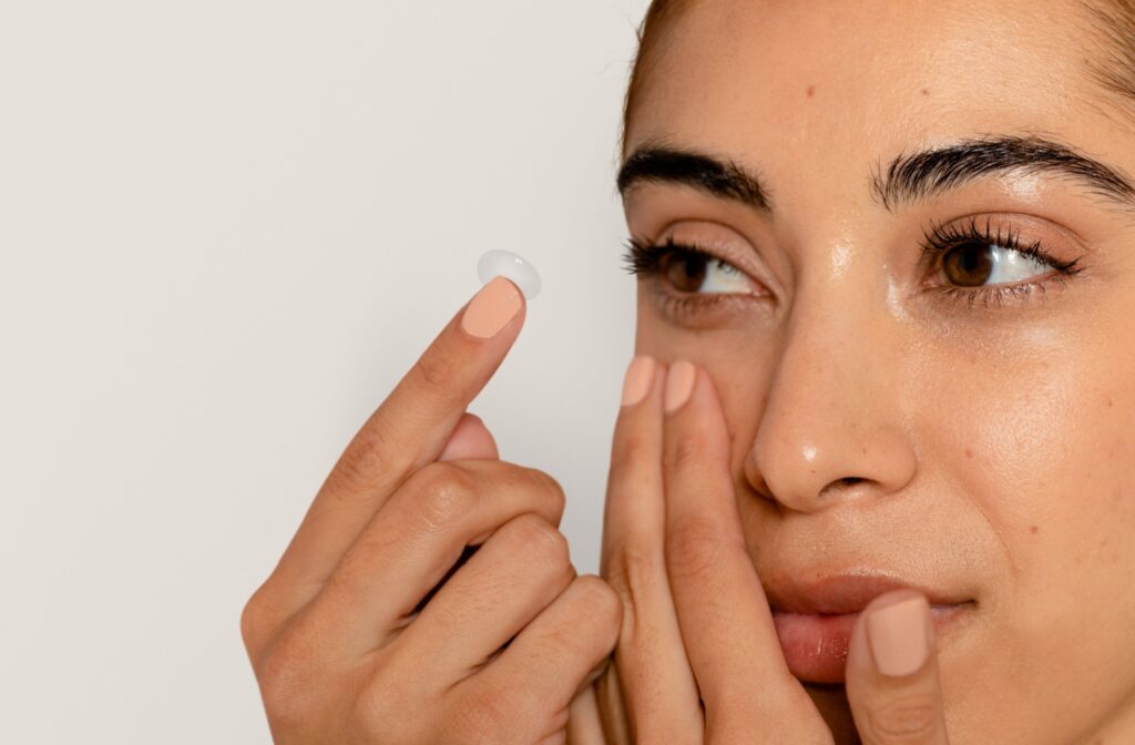 Close-up of a woman holding a contact lens on her fingertip while preparing to insert it into her eye, emphasizing proper contact lens handling and eye care.