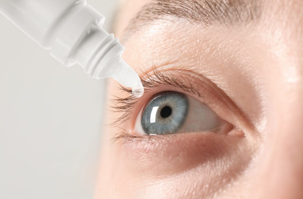 Close-up of an eye with a bottle of artificial tears about to drop onto the cornea.