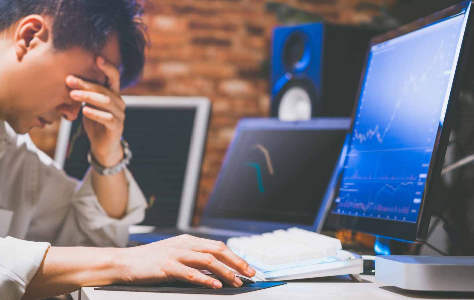 A young business person with digital eye strain rubs their sore eyes while looking at a computer screen.