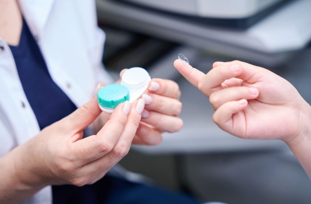 Up close photo of a clinician holding a contact lens case and another person's hand holding a contact lens on their fingertip.