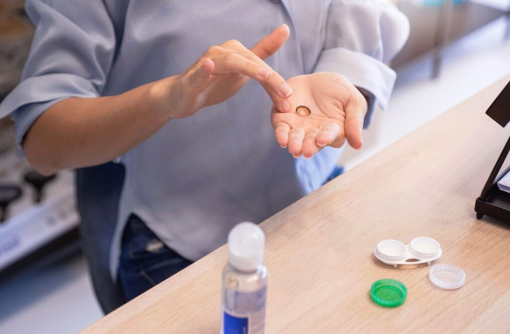 A person's hands rubbing a contact lens in one hand to clean it over a desk.