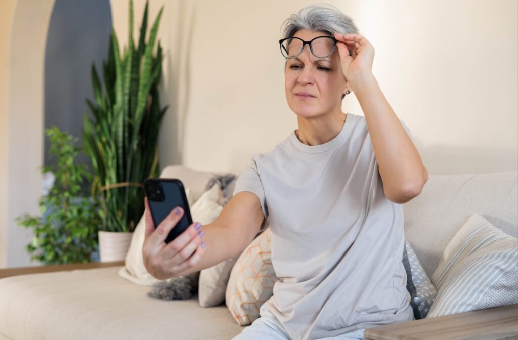 An older adult lifts up their glasses and holds their phone away from their eyes to see clearly.